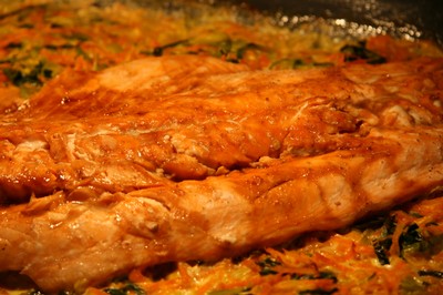 Asiatisk lax steker i ugnen på en bädd av morötter och purjolök, med smält farinsocker på toppen.